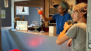 Zona de bar con mostrador, taburetes y una persona sirviendo una bebida.