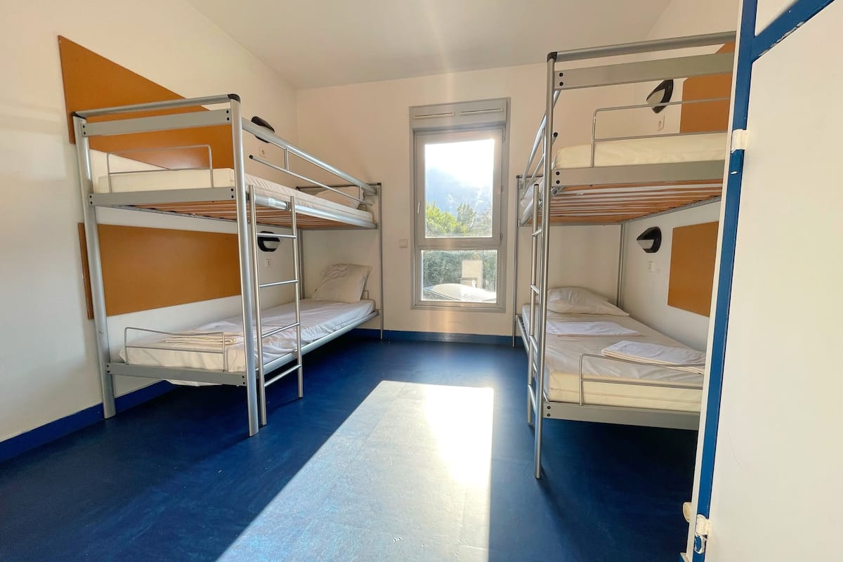A dormitory room with bunk beds, a window, and a door.