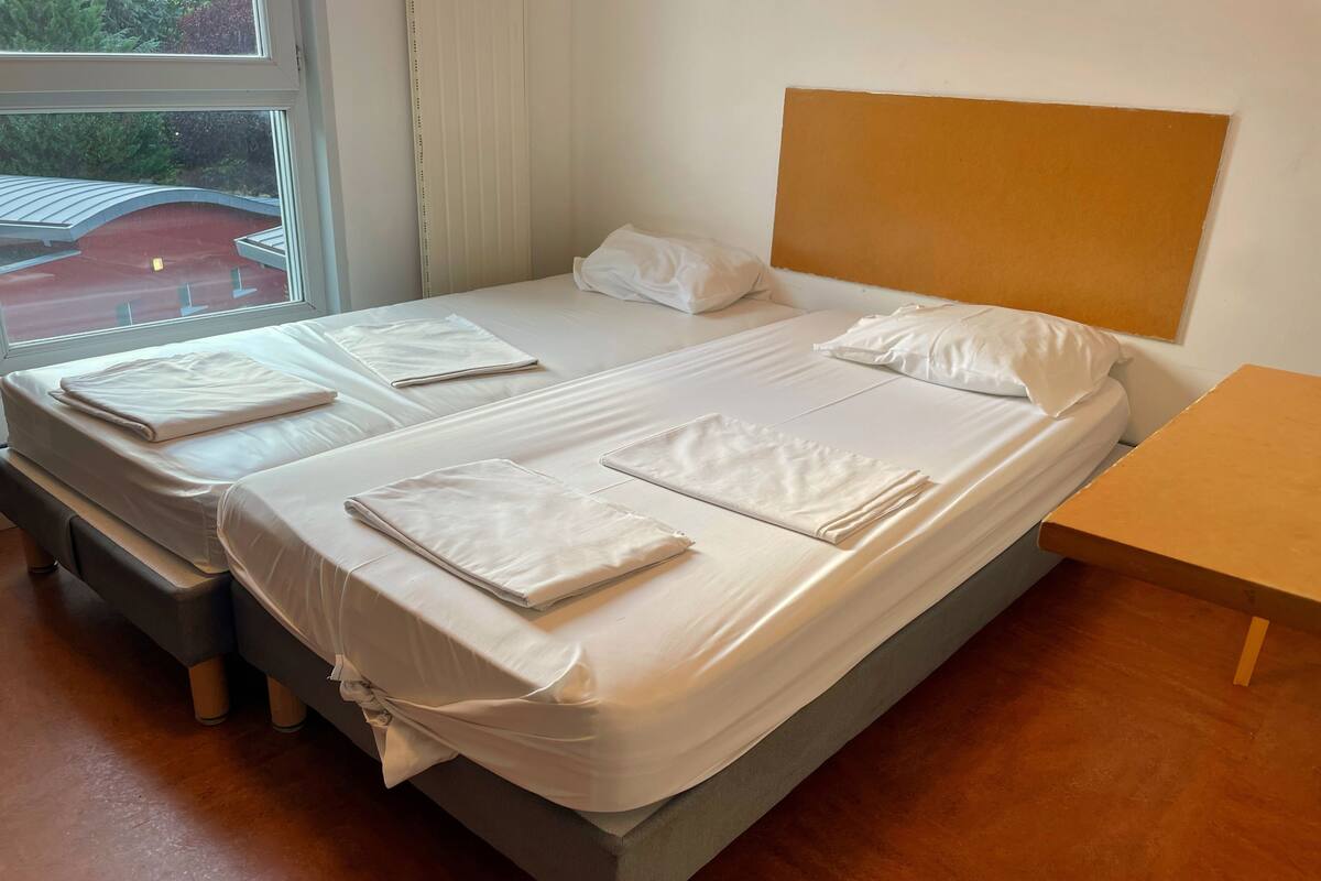 A double bed with white linens, a wooden headboard, and a small wooden table beside it.