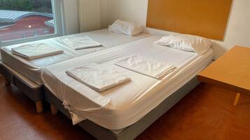 A double bed with white linens, a wooden headboard, and a small wooden table beside it.