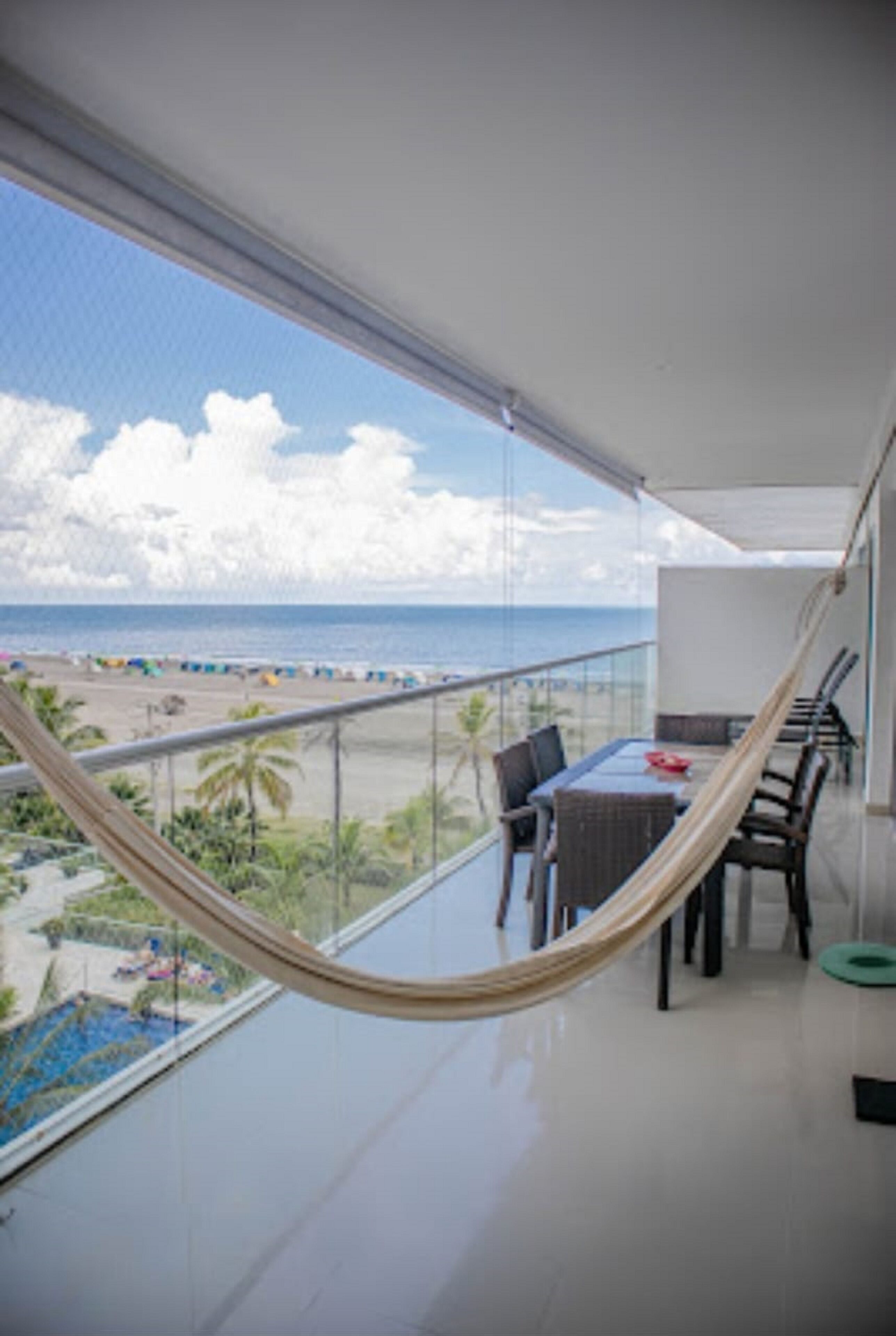 Un balcon avec vue sur la plage, un hamac et un espace repas avec des chaises et une table.