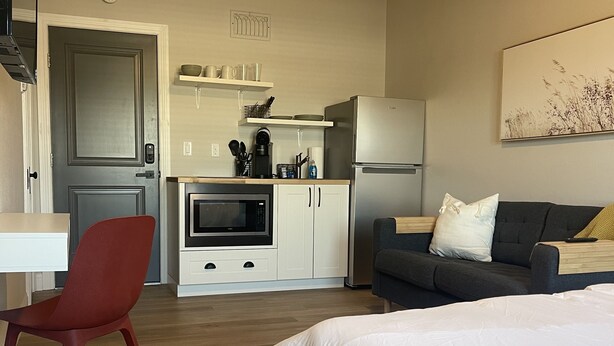 A modern hotel room with a large bed, a red chair, a kitchenette, and a gray sofa. - Apartment 202 (Cando)