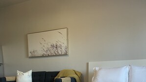 A bedroom with a large bed, a dark-colored sofa, and a wall-mounted painting. - Apartment 202 (Cando)