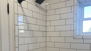 A bathroom with white subway tiles, a bathtub, a window, and a showerhead. - Apartment 202 (Cando)