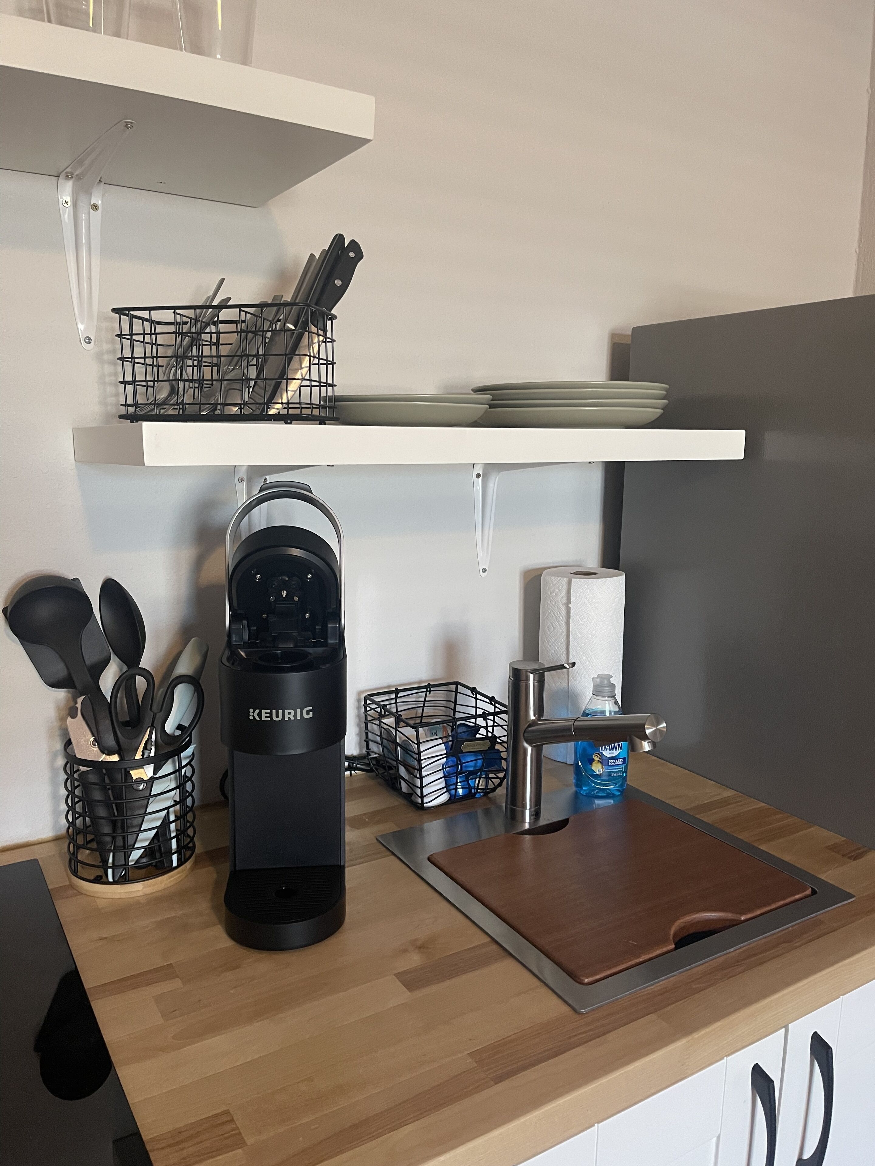 A kitchen with a Keurig coffee maker, a water dispenser, a cutting board, and various utensils.