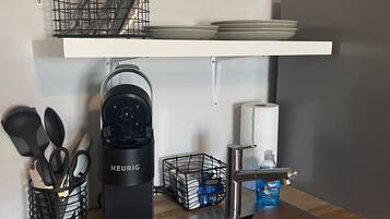 A kitchen with a Keurig coffee maker, a water dispenser, a cutting board, and various utensils.