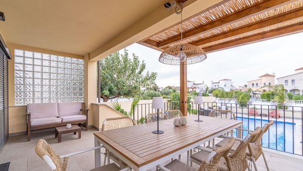 Una terraza con mesa de madera, sillas, un sofá y vista a una piscina.