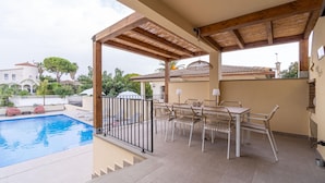 Un espacio exterior cubierto con piscina, una mesa con sillas y una pérgola.