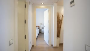 Un pasillo que conduce a un dormitorio con cama, mesita de noche, lámpara y una planta decorativa.