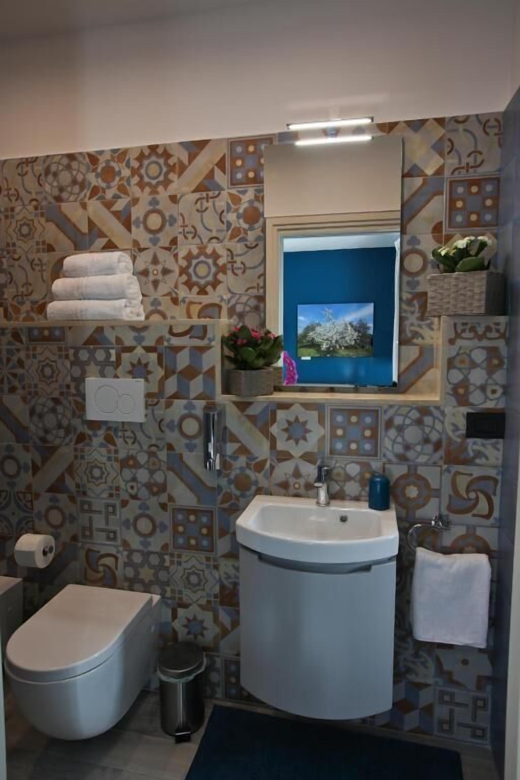 Ein Badezimmer mit Wandfliesen mit Muster, einem Waschbecken, einer Toilette und einem Spiegel.