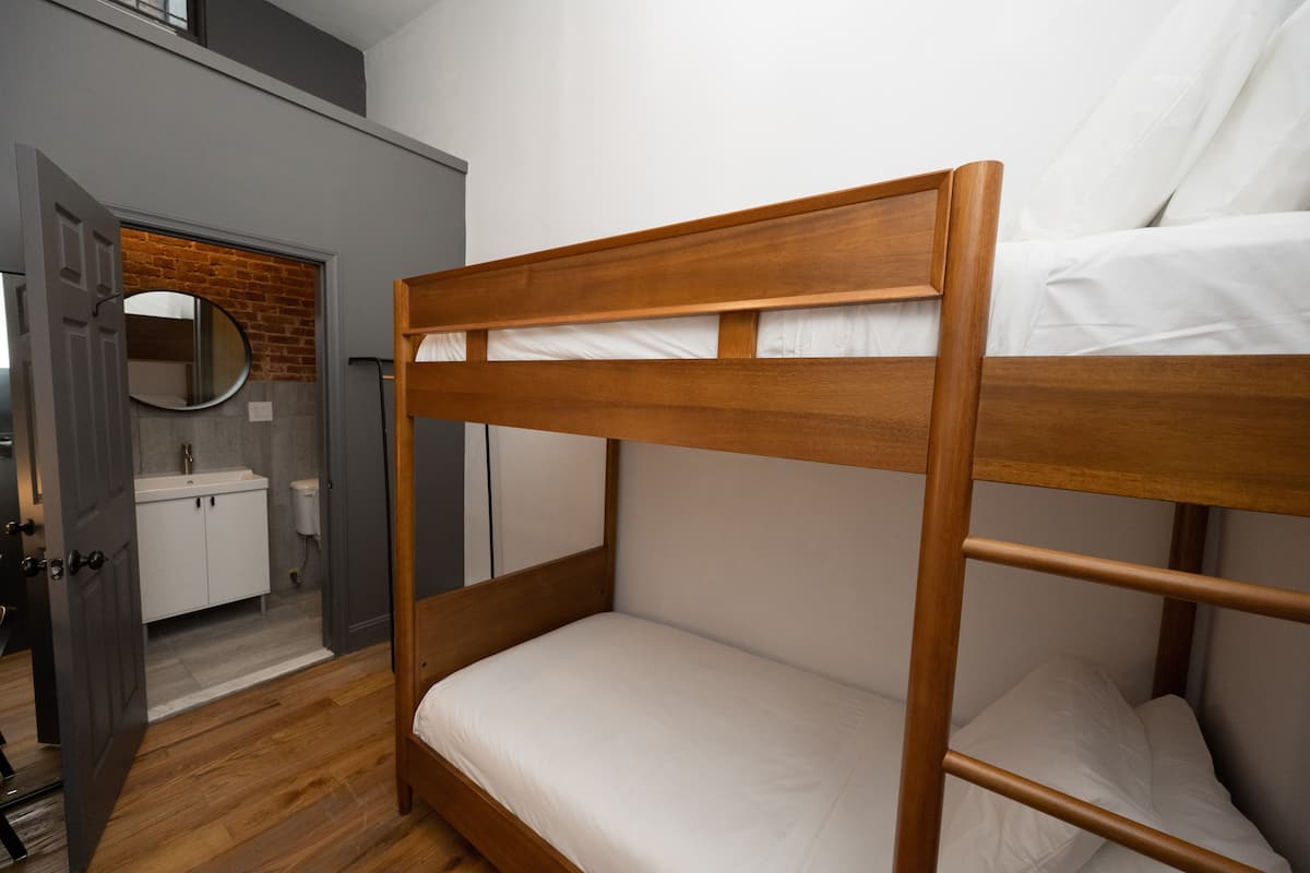 A bunk bed with a wooden frame and white bedding in a room with a gray wall and a wooden floor.