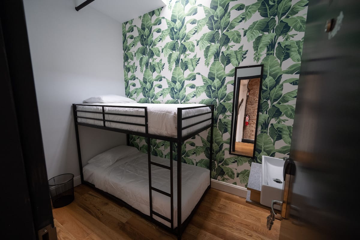 A bunk bed room with a leaf-patterned wallpaper, a small sink, and a framed picture on the wall.