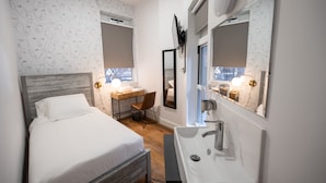 A bedroom with a bed, a desk, and a bathroom with a sink and mirror. - The Flat NYC (New York)