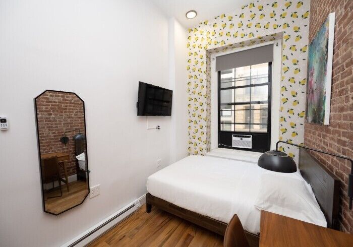 A bedroom with a bed, a TV mounted on the wall, a window with a view, and a mirror.