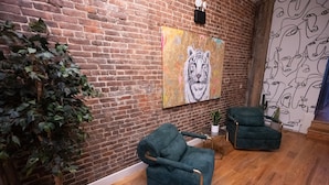 A room with a brick wall, a large tiger painting, a green armchair, a potted plant, and a wooden floor. - The Flat NYC (New York)