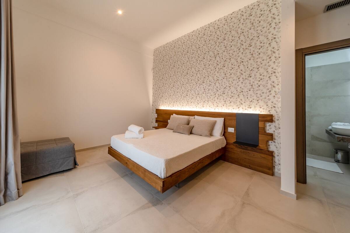Un dormitorio moderno con una cama de madera, un banco gris y un papel tapiz estampado.