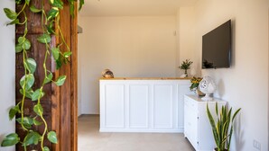 A clean, modern kitchen with white cabinetry, a wooden countertop, and a flat-screen TV mounted on the wall. - Sarmenti Agriresort (Otranto)