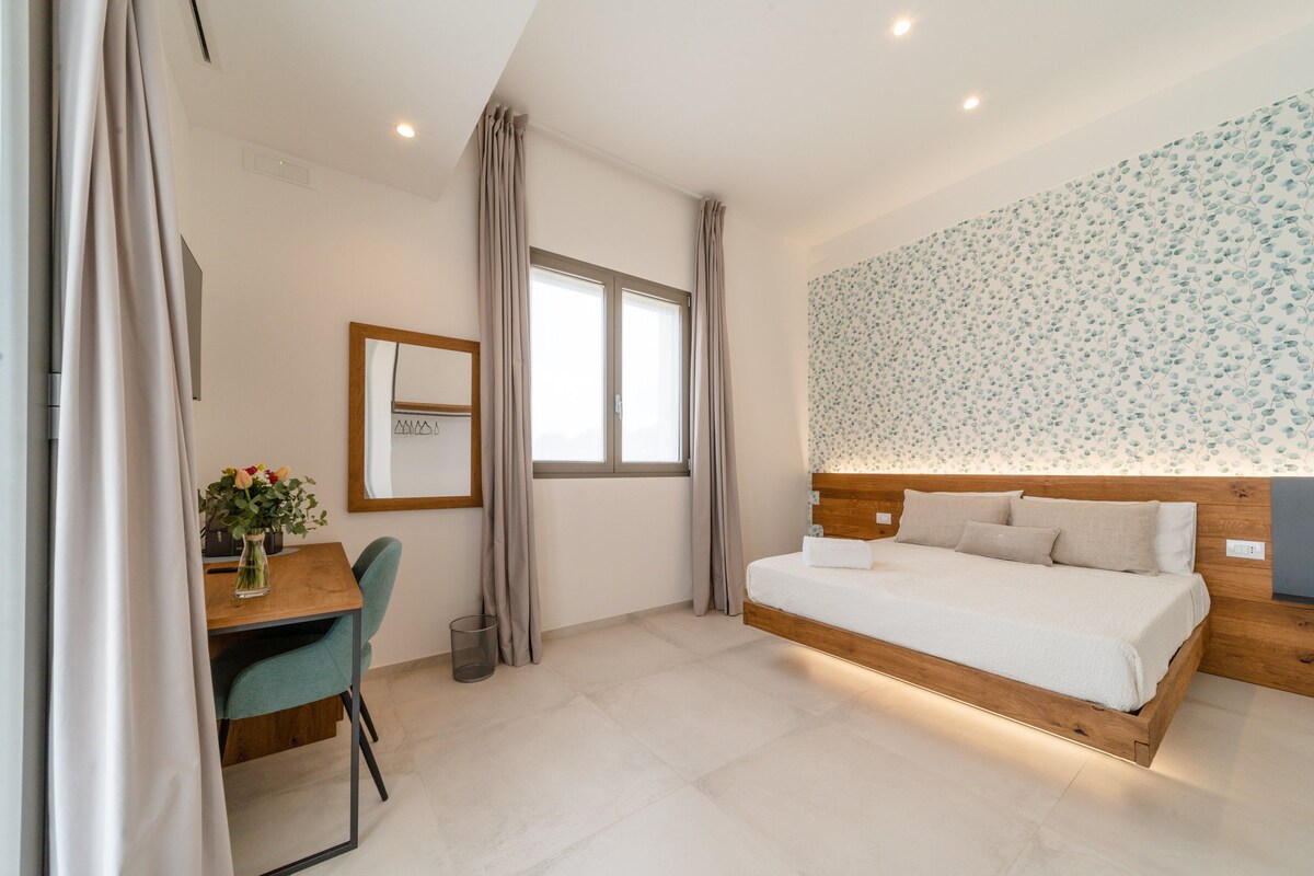A modern bedroom with a wooden bed, a desk with a chair, and a window with curtains.