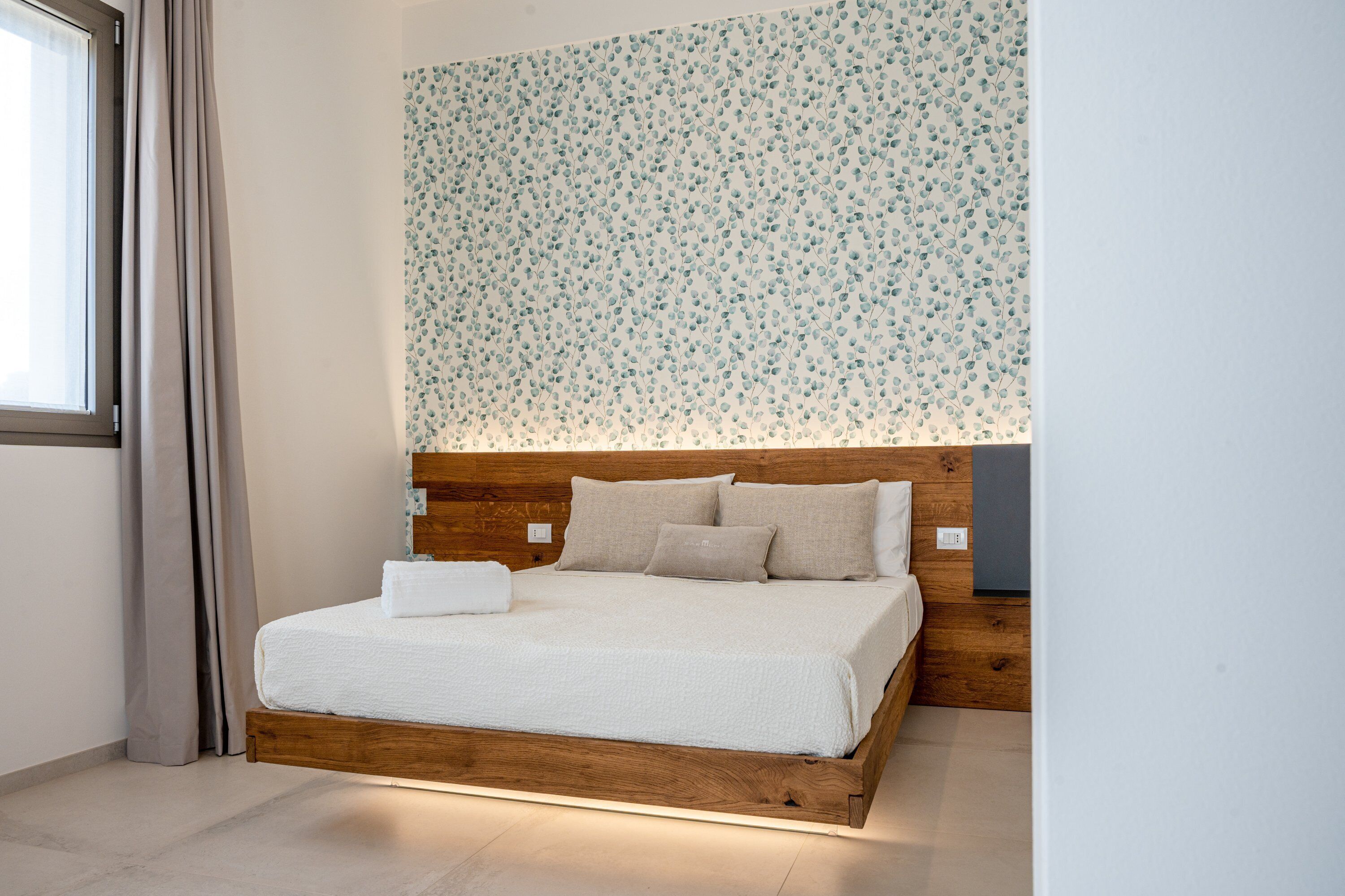 Une chambre à coucher avec un cadre de lit en bois, une tête de lit à motifs floraux et un couvre-lit blanc.