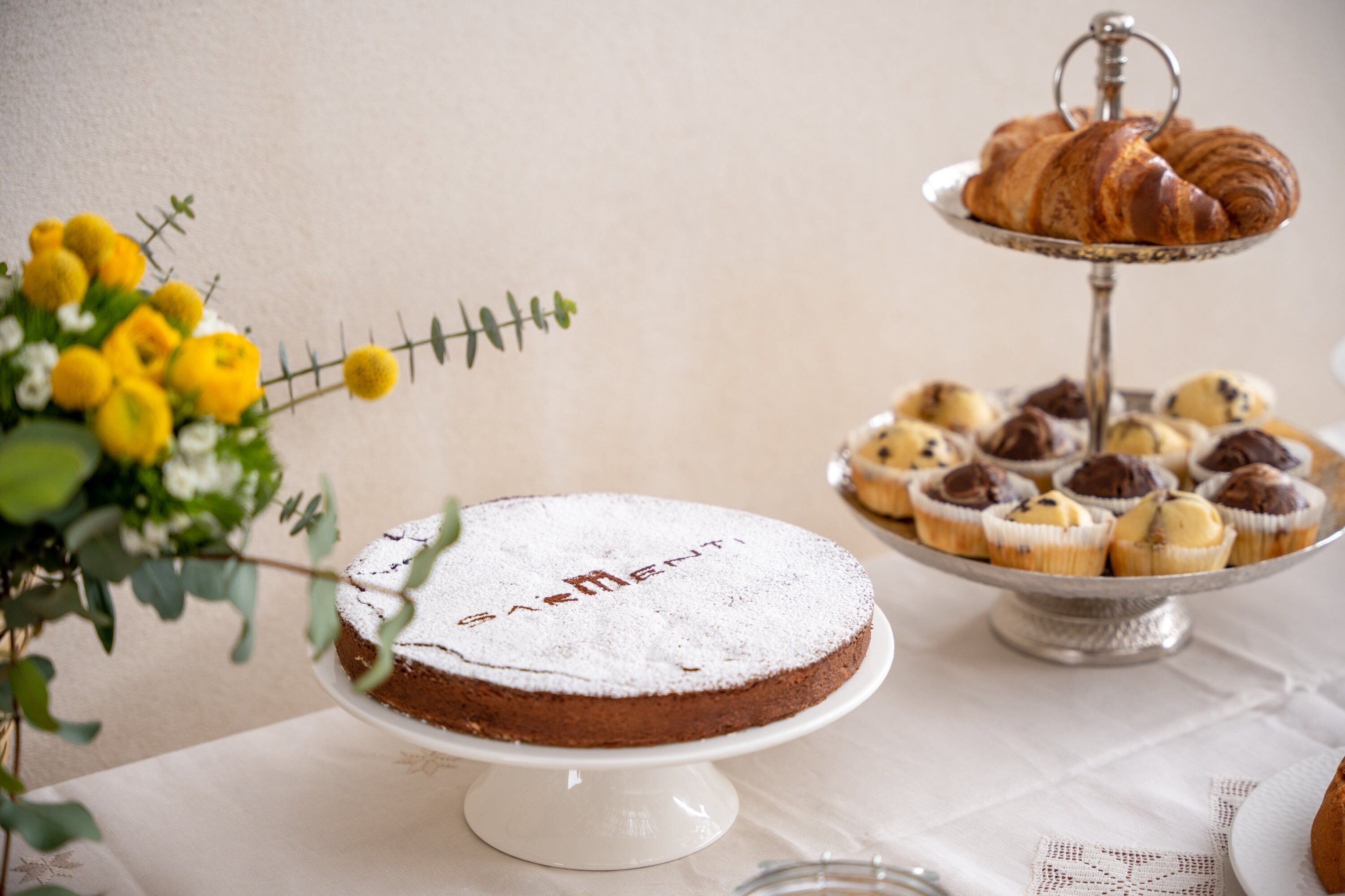 Una mesa de postres con pastel, cupcakes y croissants.