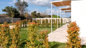 A modern outdoor area with a stone wall, a wooden pergola, and a pathway leading to a white building. - Sarmenti Agriresort (Otranto)