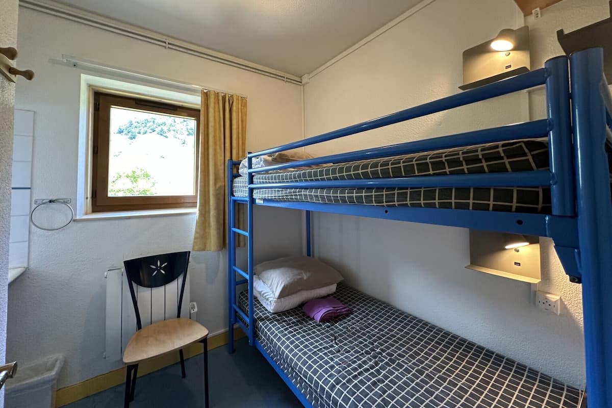 A bunk bed room with a window, chair, and wall-mounted shelf.