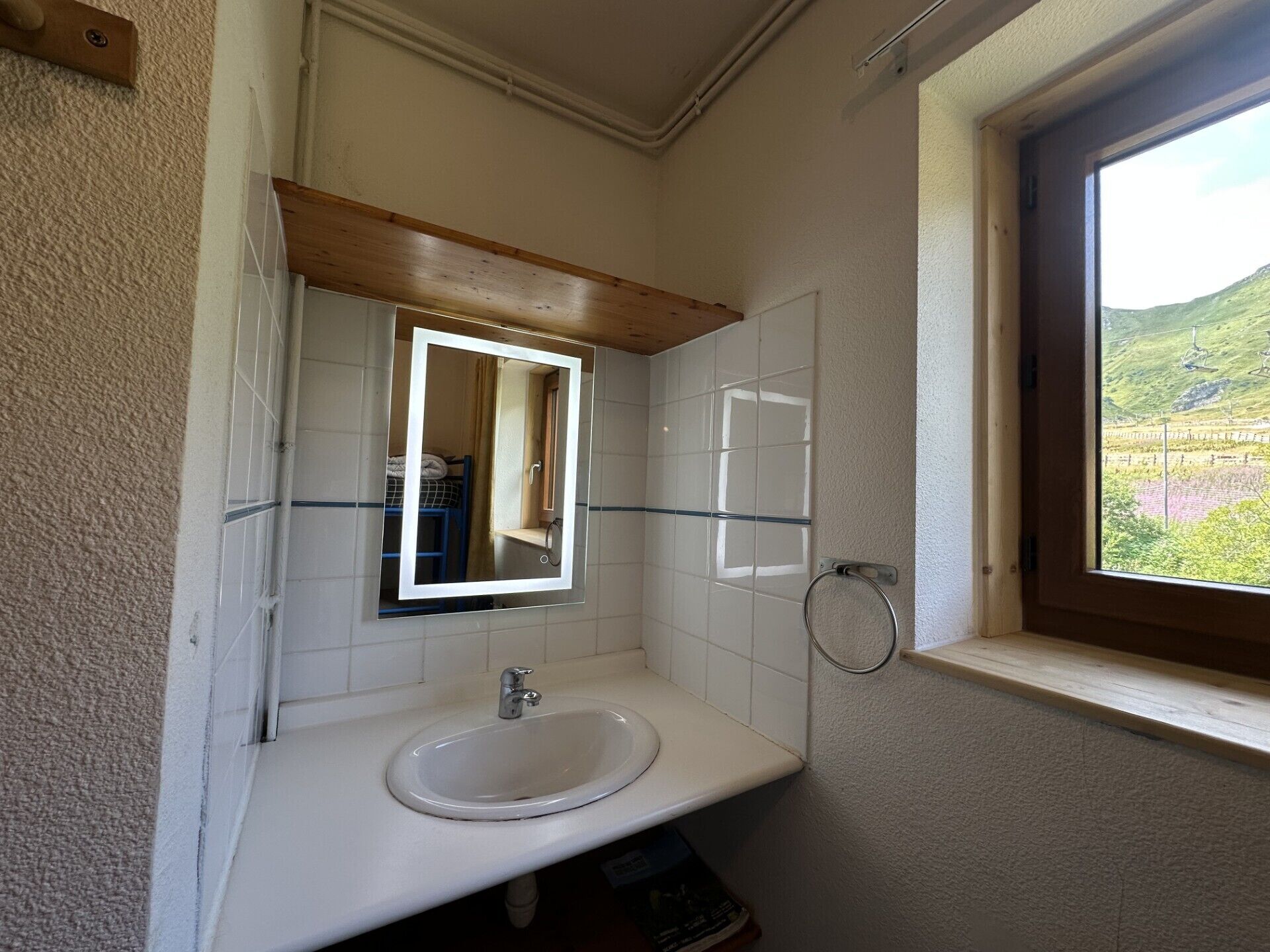 Un baño con un lavabo blanco, un espejo y una ventana con vistas a un paisaje verde.