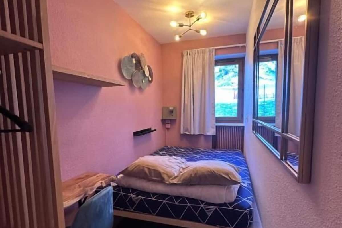 A narrow room with a bed, a desk, and a window.