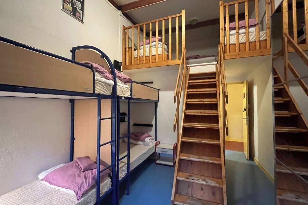 A dormitory room with bunk beds, a wooden staircase, and a door.