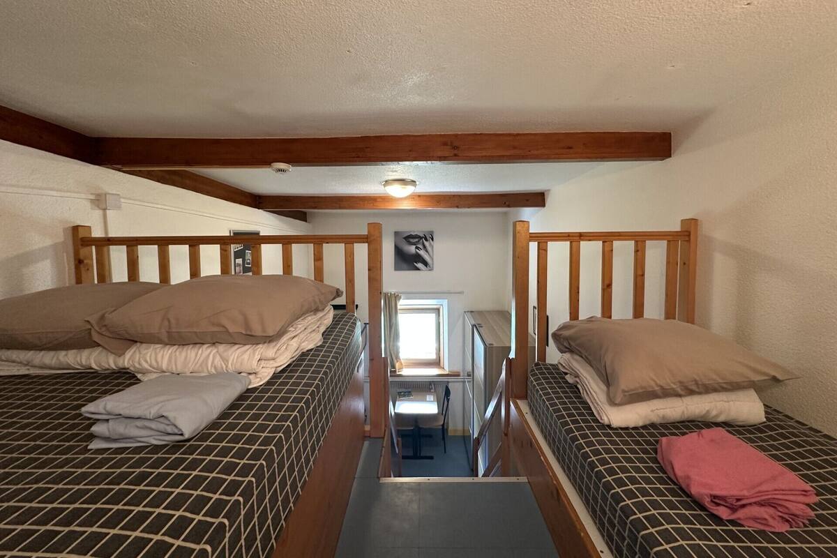 A small, cozy room with two bunk beds, a wooden ceiling, and a simple layout.