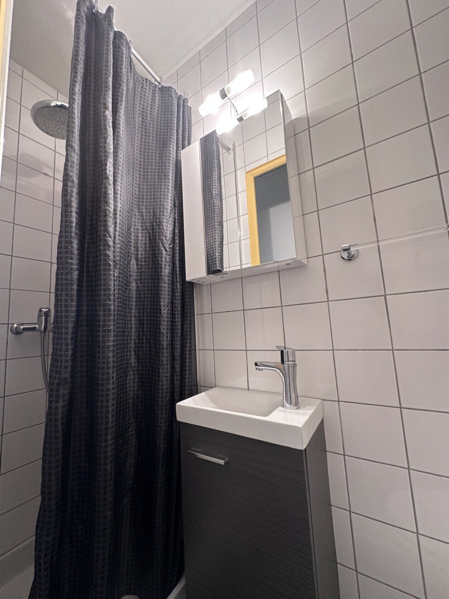 A bathroom with a shower curtain, a mirror, a sink, and tiled walls.