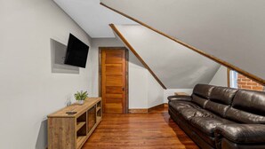 A loft bedroom with a sloped ceiling, a wooden door, a leather sofa, and a small wooden console table.