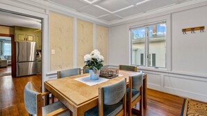 A dining area with a wooden table and chairs, a vase with flowers, and a view of the outside through a window.