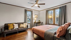 A hotel room with a bed, a sofa, a desk, a chair, and large windows.