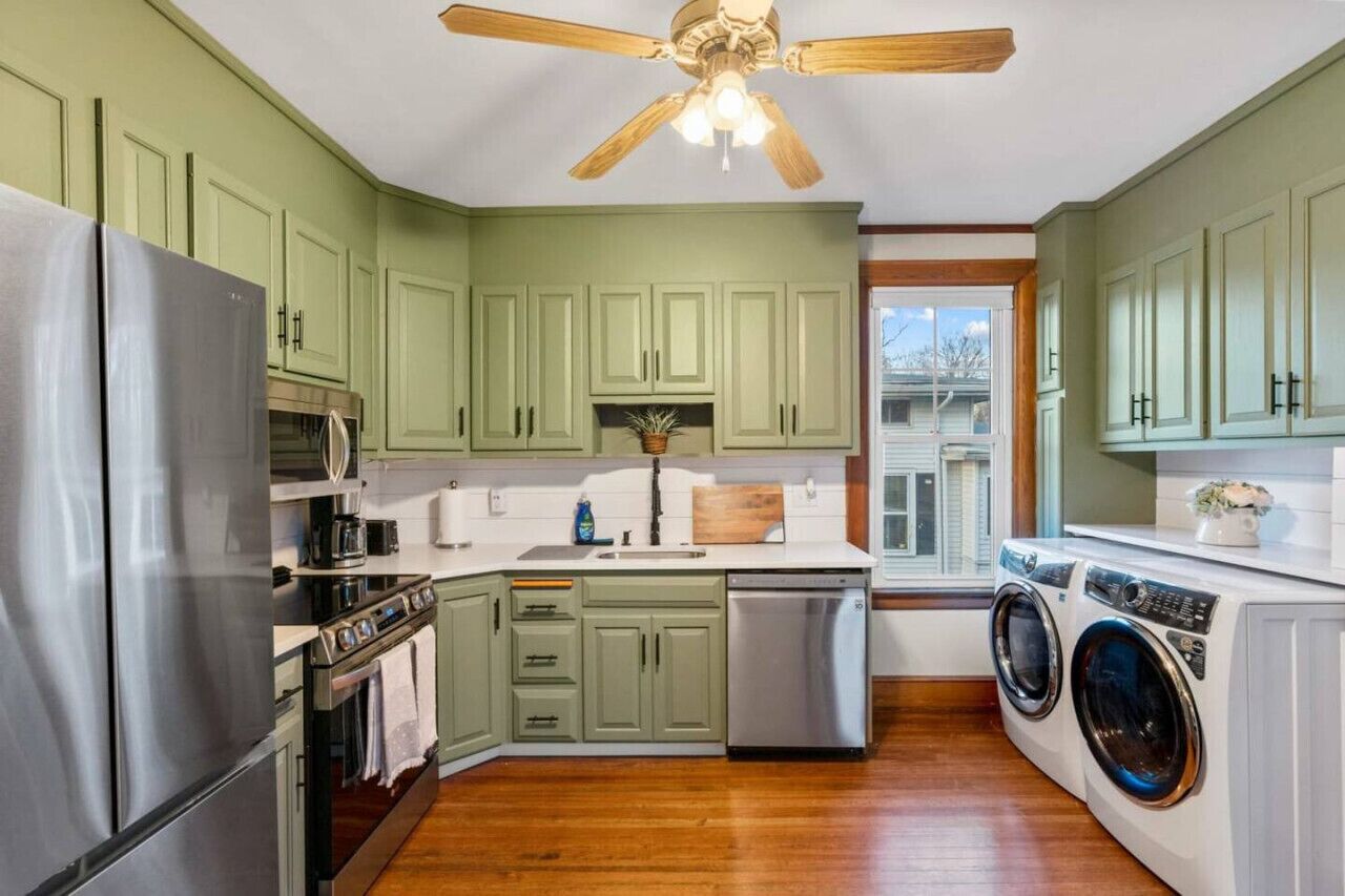 A kitchen with green cabinets, stainless steel appliances, a ceiling fan, and a view to the outside.
