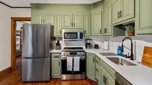 A kitchen with green cabinets, stainless steel appliances, a double sink, and a wooden ceiling fan.