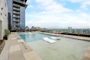 Relax by the rooftop pool surrounded by lounge chairs and sun loungers, offering a panoramic view of the city.