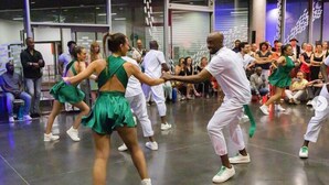 Een dansvoorstelling in een ruime hal met modern design, met een gepoetste vloer en een groot publiek dat rondom de zaal zit.