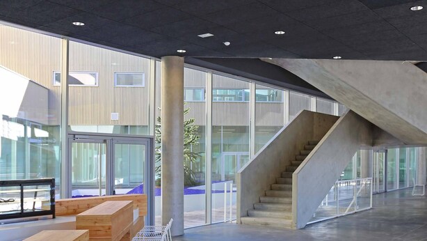 Een ruime lobby met een moderne trap, houten zitplaatsen en een glazen balustrade.