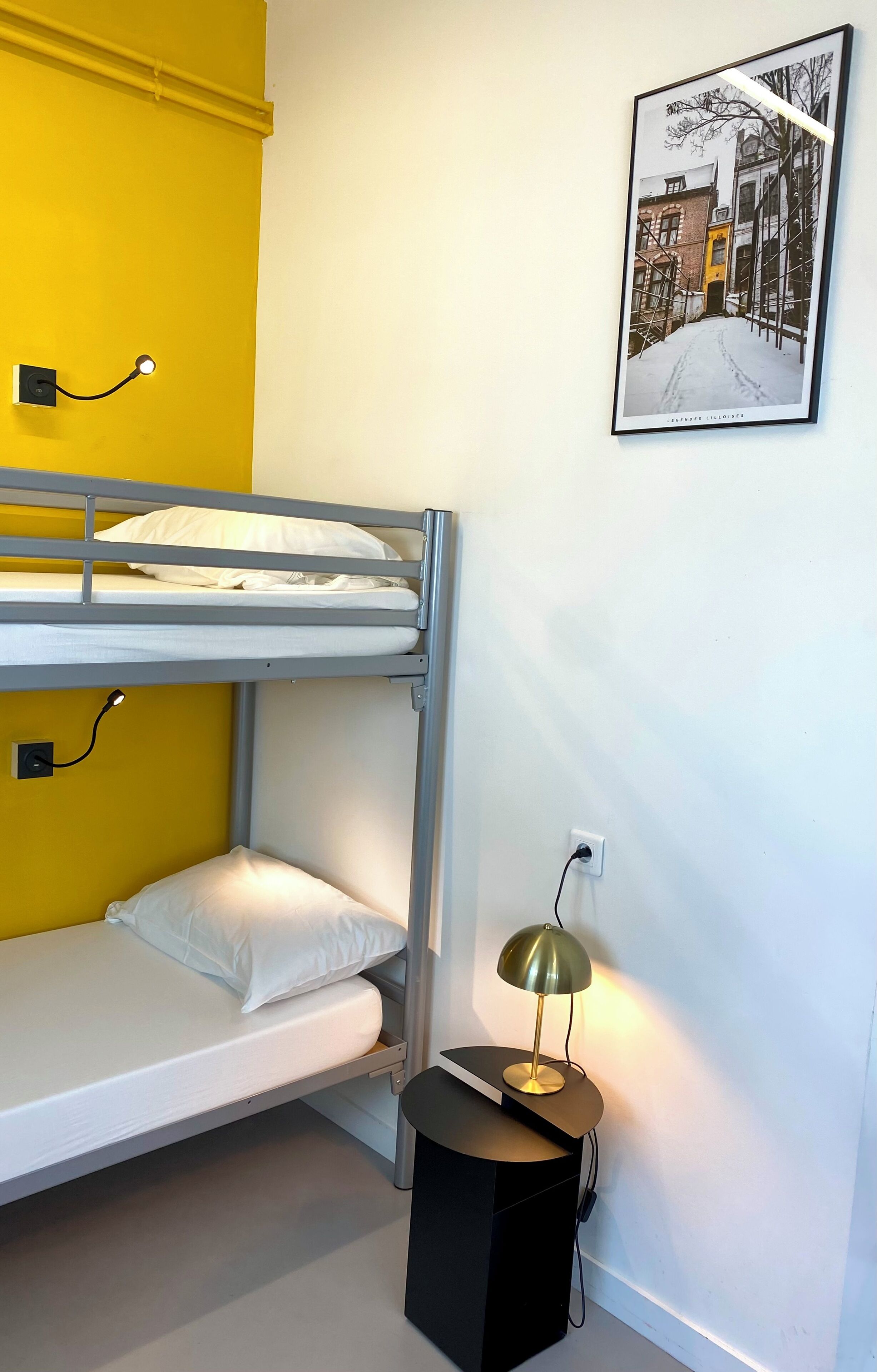 A bunk bed with a white mattress, a black side table with a lamp, and a framed picture on the wall.