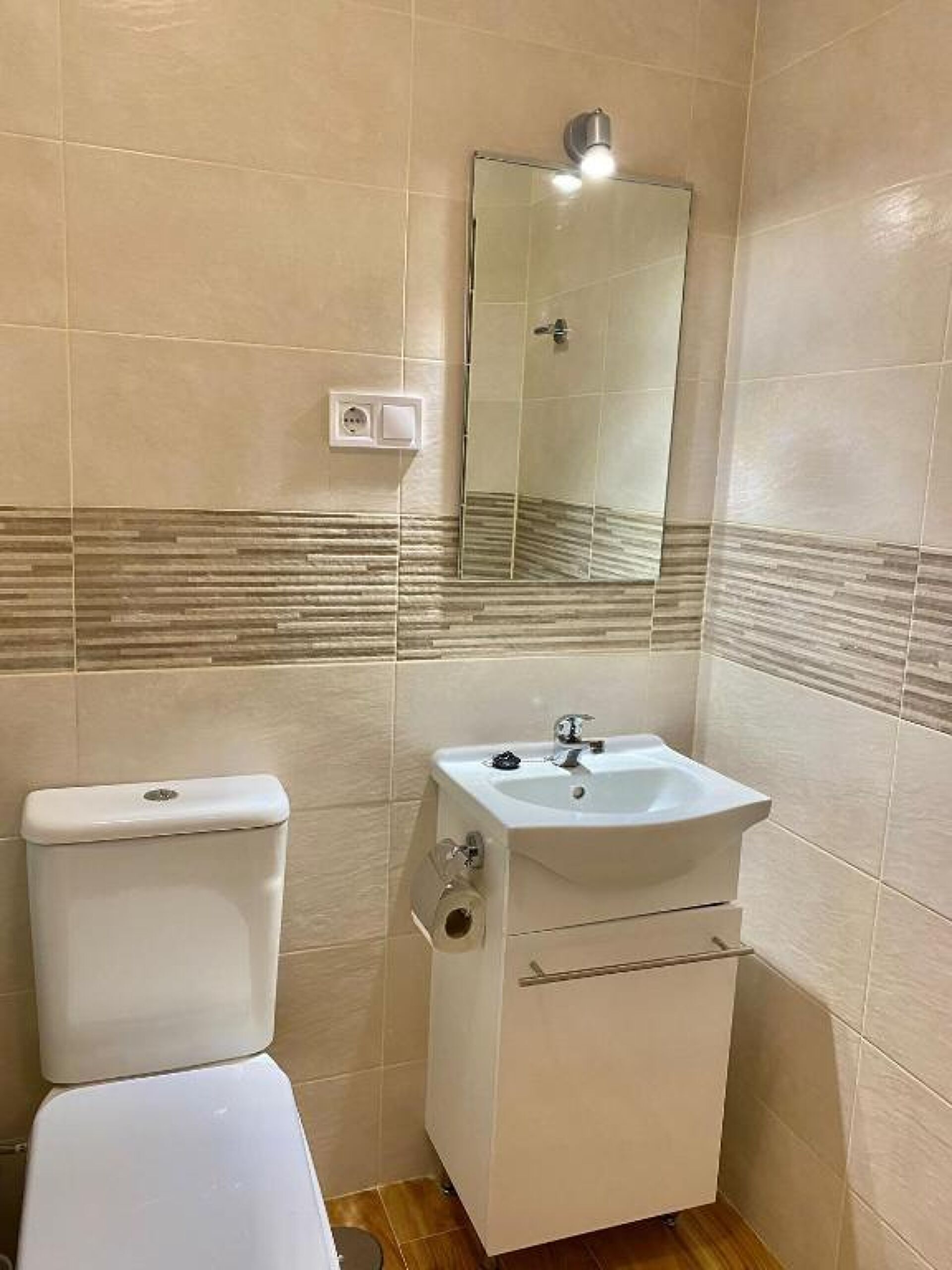 Une salle de bain équipée de toilettes, d’un lavabo, d’un miroir et de murs carrelés.
