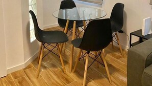 A small dining area with a glass table and four chairs, a window with blinds, and a wall-mounted air conditioner. - Mirasierra Center - Metro Usera 02 (1 bedroom apartment) (Madrid)