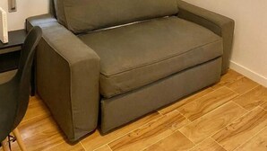 A room with a grey sofa, a small table, and a window with blinds. - Mirasierra Center - Metro Usera 02 (1 bedroom apartment) (Madrid)