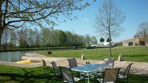 An outdoor seating area with a table and chairs, a small pond, and a stone building in the background. - La Maison Du Canal (Clamerey)