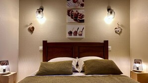A neatly made bed with a wooden headboard, two green pillows, and a textured blanket. There are wall-mounted light fixtures on either side of the bed, and two heart-shaped decorations hanging on the wall. - La Maison Du Canal (Clamerey)