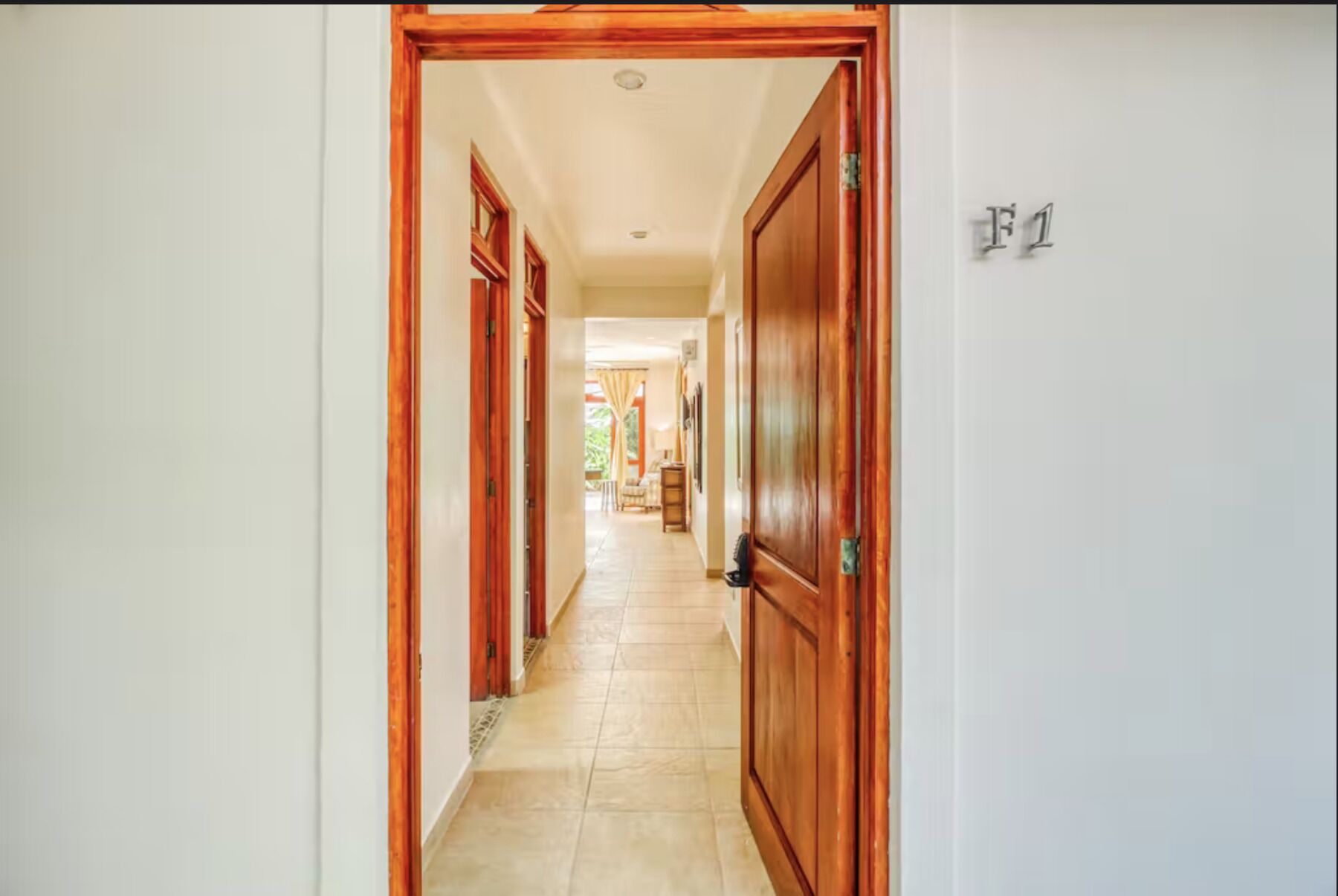 A hallway with wooden doors and a tiled floor, leading to a room with a window.