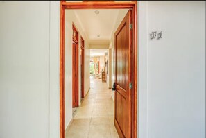 Un pasillo con puertas de madera y suelo de baldosas, que conduce a una habitación con ventana.