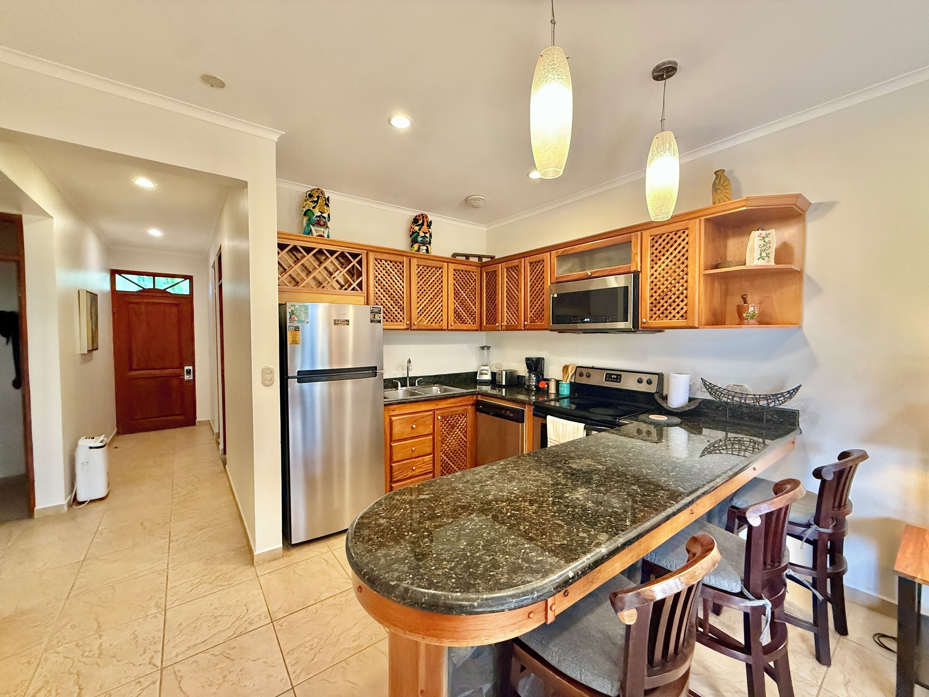 A modern kitchen with a central island, stainless steel appliances, wooden cabinets, and pendant lighting.