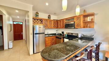 A modern kitchen with a central island, stainless steel appliances, wooden cabinets, and pendant lighting.