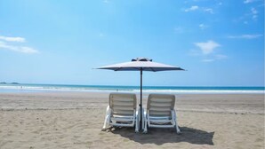 Een strand met twee witte ligstoelen onder een grote parasol.